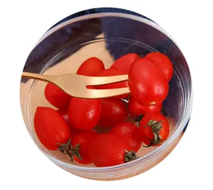 Gouden roestvrijstalen dessertvork die een cherrytomaatje in een glazen kom prikt.