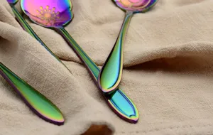 Close-up detail of rainbow titanium-plated floral dessert spoons on soft beige fabric background.
