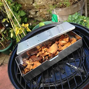 Stainless steel BBQ smoker box on a grill grate with natural wood chips for meat smoking