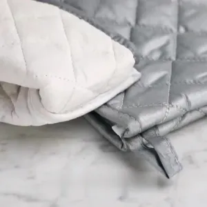 Detailed close-up showing the quilted texture of heat-resistant oven mitts in white and grey