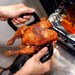 Hand using black meat shredder claws to lift a whole roasted chicken out of oven.