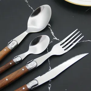 Detail of wood-handled stainless steel Laguiole-style cutlery set on dark marble.