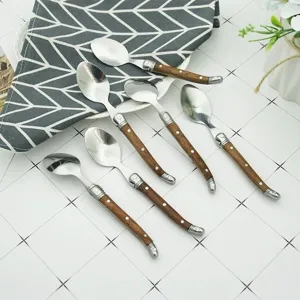 Set of Laguiole style spoons with rustic wooden handles on a white grid surface