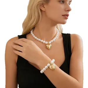 Elegante set di collana e bracciale di perle con ciondolo a cuore dorato su modella.