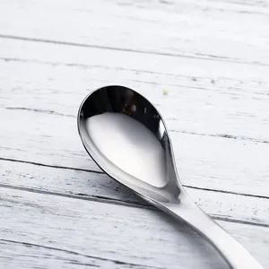 Close-up detail of a polished stainless steel soup spoon on a white wooden background