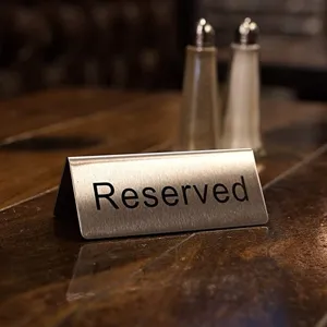 Close-up van een rvs 'Reserved' bordje op een houten tafel in een restaurantsetting.