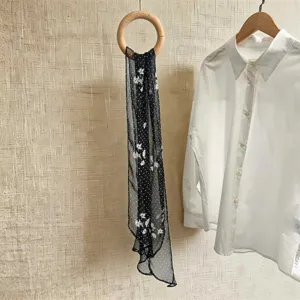 Nahaufnahme eines schwarzen Seidenschals mit eleganten weißen Blumen- und Polka-Dot-Mustern
