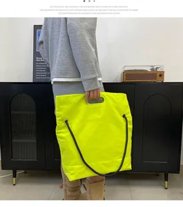 Detail shot of a large neon yellow nylon tote bag held by a model indoors.