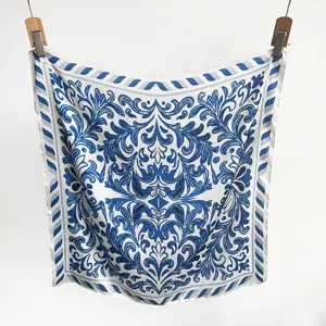 Detailed macro shot of the elegant blue baroque pattern on a white silk-like square scarf.