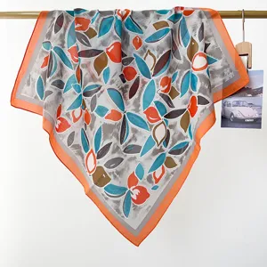 Detailansicht eines leichten Baumwoll-Quadrattuchs mit leuchtend orangen und blauen Blattmustern.