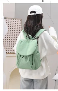 Rear view of a light green nylon travel backpack shown on a model in a white sweatshirt