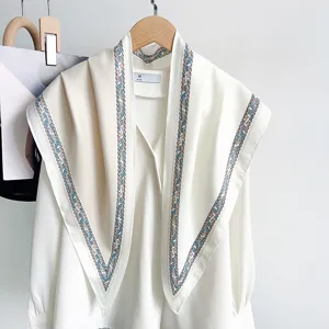 Vue détaillée d'un grand foulard triangulaire avec bordure géométrique sur un chemisier blanc