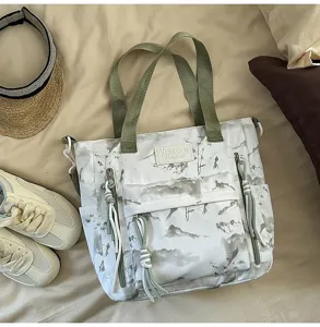 Close-up detail of a white landscape print tote bag with olive green straps and zippers