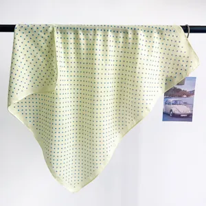 Detail of a light yellow square scarf with blue polka dots hanging on a black rod