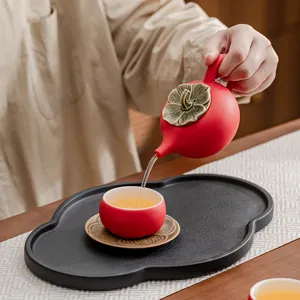 Elegant persimmon-shaped red ceramic tea set with teapot, cup, and a black tray.