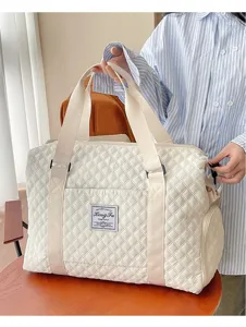 Bolso de viaje acolchado grande crema sostenido por modelo en un ambiente interior