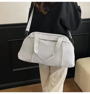 Back view of a large light grey travel bag worn as a shoulder bag by a model.