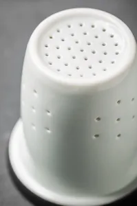 Macro view of the white ceramic tea filter showing detailed drainage holes for leaf separation.