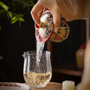 Elegante gaiwan de esmalte estilo palacio vertiendo té en una jarra de cristal fina.
