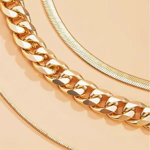 Close-up detail of a 3-piece punk style gold curb and snake bone chain necklace set.