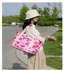 Grote roze reistas met luipaardprint gedragen door een model in een zonnig park.