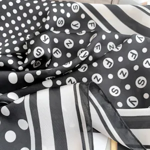 Primo piano di un foulard in seta bianco e nero a pois e strisce che mostra la trama del tessuto