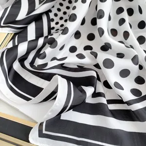 Dettaglio ravvicinato di un lussuoso foulard in seta bianco e nero a pois e righe.