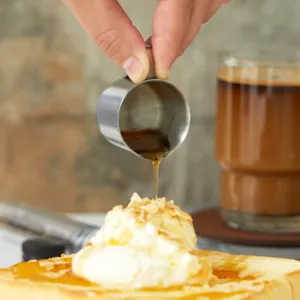 Mini Milchkännchen aus Edelstahl gießt süßen Honigsirup über feines Eiscreme-Toast-Dessert