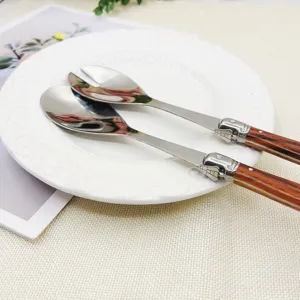 Laguiole-Salatbesteck aus Edelstahl mit Holzgriffen auf einem weißen Teller, Detailaufnahme