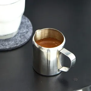 Nahaufnahme von dem Edelstahl-Milchkännchen mit Espresso auf minimalistischem Tisch