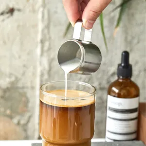 Detail eines Milchkännchens aus Edelstahl, das Milch in einen Kaffeebecher gießt