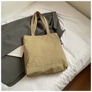 Sac fourre-tout en nylon kaki sur un drap blanc avec un manteau gris et un livre