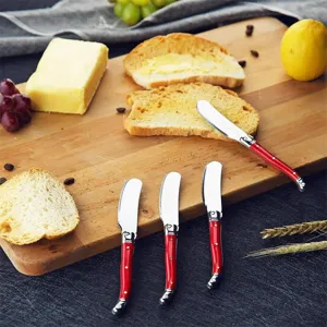 Detail of Laguiole style stainless steel butter knives with red handles on wood