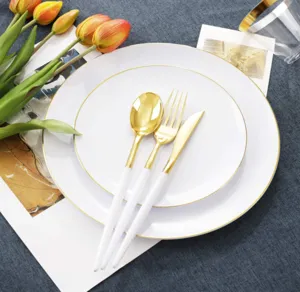 Weiße Kunststoffteller mit Goldrand und weiß-goldenes Besteckset auf blauem Tischtuch