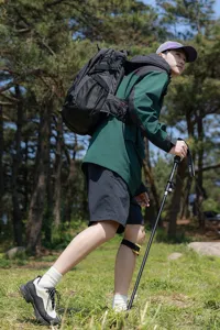 Man met een grote zwarte professionele outdoor rugzak tijdens een trekking in een zonnig bos