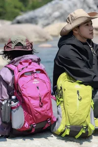 Outdoorliefhebbers met roze en limoengroene wandelrugzakken bij een rivier in de natuur.
