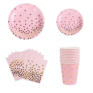 Set di stoviglie rosa per feste con piatti, bicchieri e tovaglioli a pois dorati.