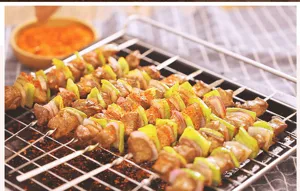 Nahaufnahme flacher Edelstahl-Grillspieße mit gegrilltem Fleisch und Paprika auf dem Rost