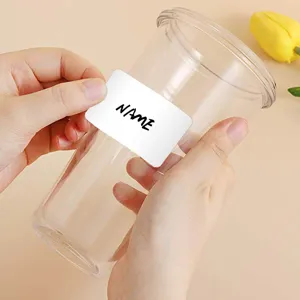 Macro view showing a hand applying a white writable name label sticker onto a clear glass cup