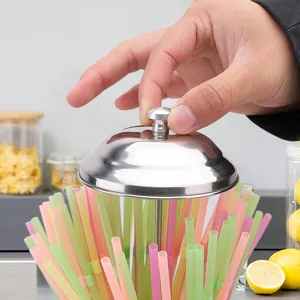 Nahaufnahme, wie eine Hand den Edelstahldeckel eines Glas-Strohhalm-Spenders anhebt