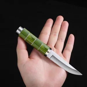 Primer plano de un cuchillo de exterior afilado con mango de madera verde en mano.