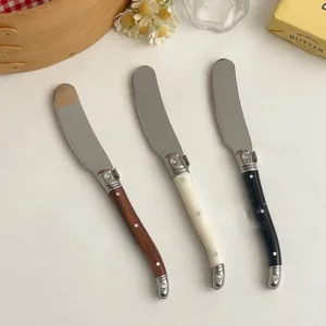 Detailed shot of three stylish butter knives featuring wooden, white and black handles.