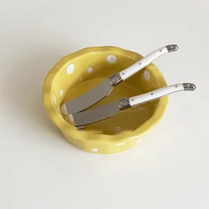 Yellow polka dot ceramic bowl set with two white handle butter knives, elegant tabletop detail.