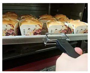 Chrome-plated metal oven rack gripper with insulated handle pulling a hot baking tray