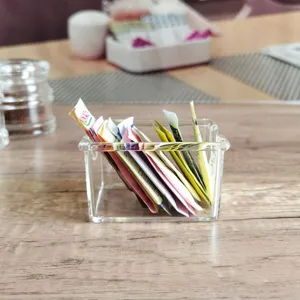 Detailopname van een heldere rechthoekige acrylnouder met diverse suiker- en theezakjes