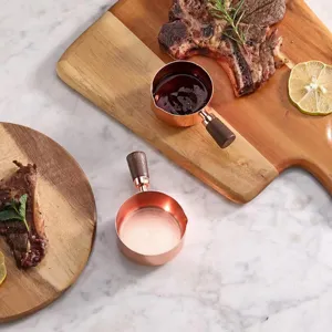 Rose gold stainless steel measuring cups with walnut wood handles on a marble table