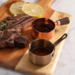 Detail of rose gold and brass sauce cups with walnut handles on a wooden board
