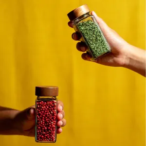 Gros plan d'un bocal à épices carré en verre avec couvercle en bois et herbes.