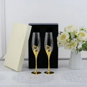 Close-up of elegant gold wedding champagne flutes with crystal heart design and gift box.
