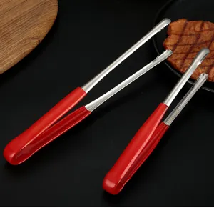 Close-up of stainless steel BBQ tongs with red handles on a dark surface